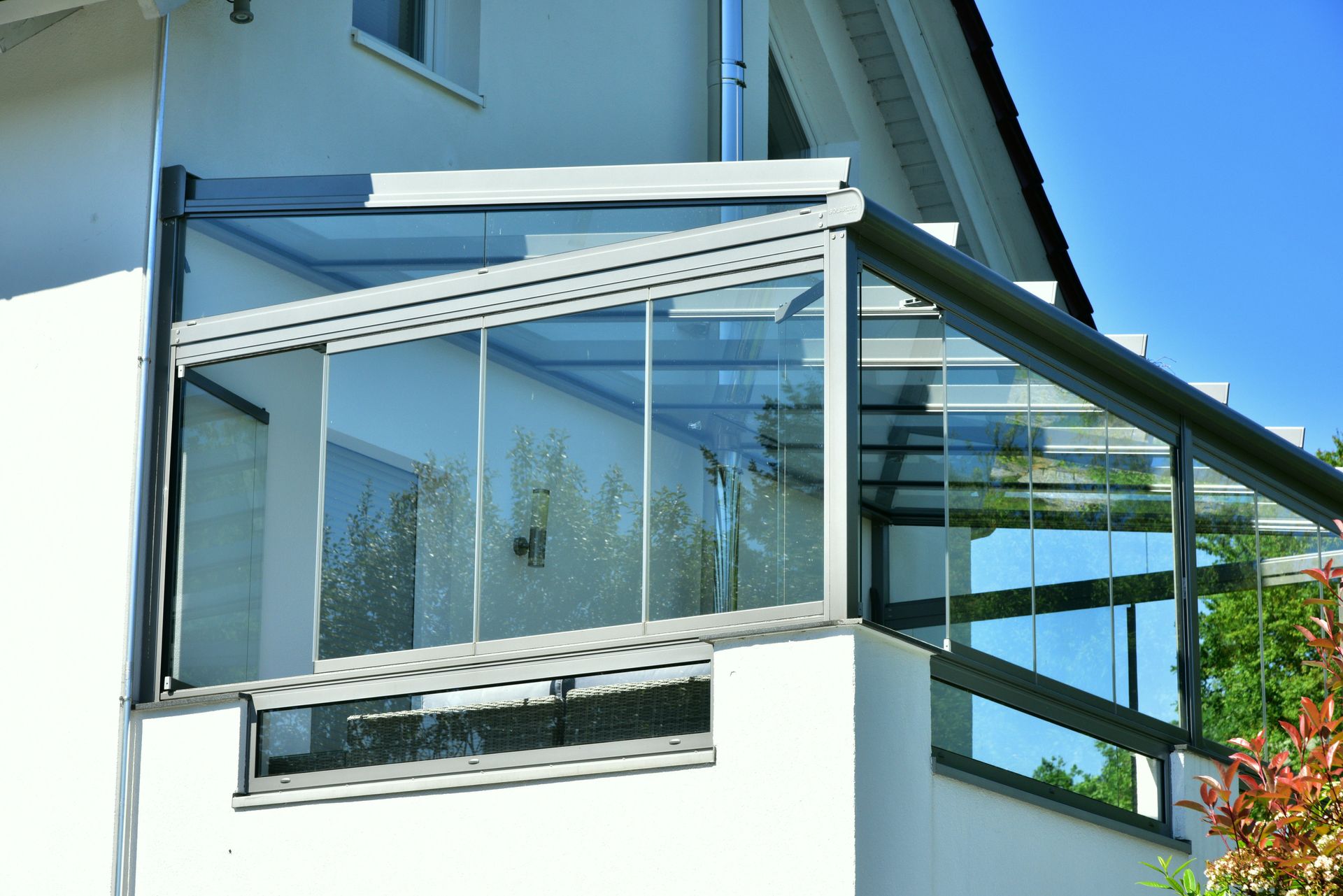 Balcon vitré avec toit transparent et portes coulissantes en verre, attenant à un bâtiment blanc.
