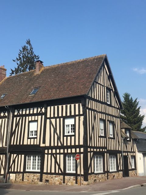 Maison à colombages avec poutres noires et remplissage blanc, toit brun et petites fenêtres, à un coin de rue, ciel bleu.