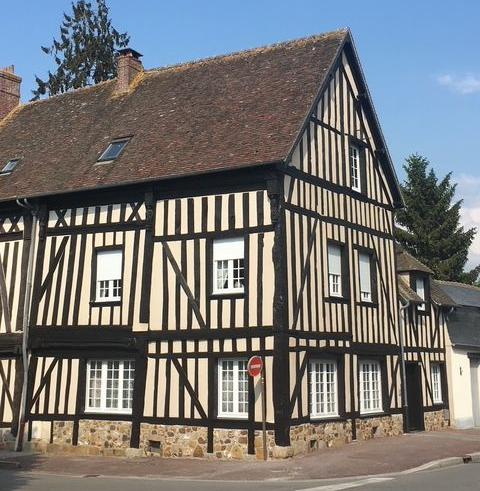 Bâtiment à colombages noir et blanc avec soubassement en pierre et toit brun, vue d'angle, journée ensoleillée.
