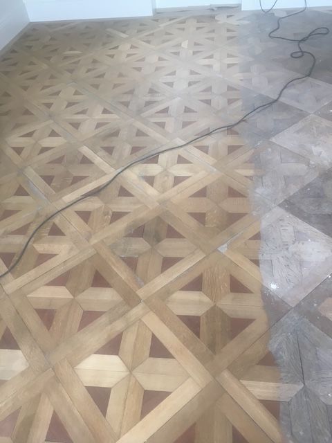 Parquet en bois à motif géométrique répétitif, partiellement rénové avec un contraste visible.