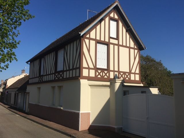 Bâtiment de deux étages avec un premier étage en stuc beige clair et un deuxième étage en colombages ; finitions marron.