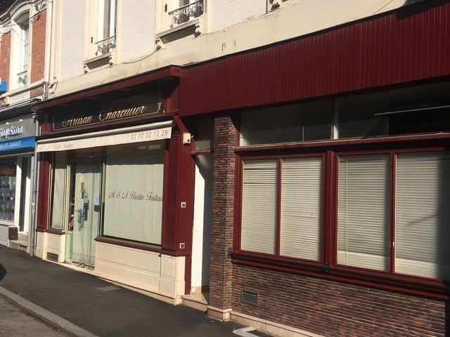 Façade avec encadrement bordeaux, auvent blanc et grandes vitrines. Inscription sur l'auvent.