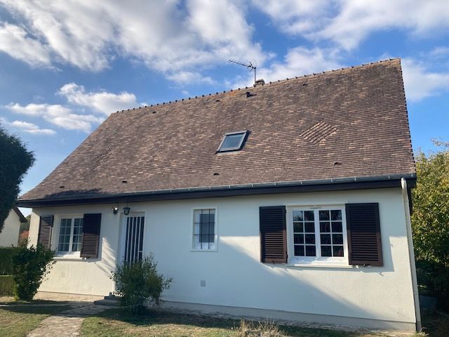 Maison blanche au toit marron et aux volets, sous un ciel bleu.