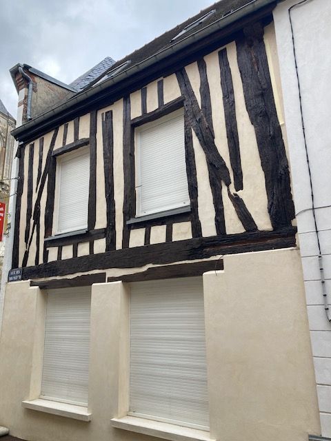 Bâtiment à colombages avec poutres en bois sombre, remplissage blanc et volets fermés.