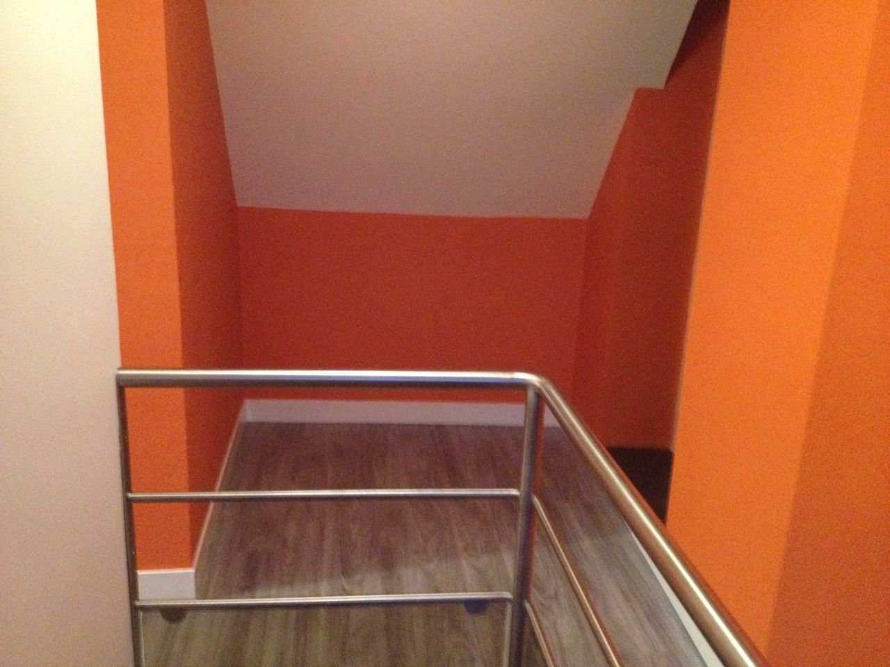 Alcôve peinte en orange avec une rambarde en métal. Sol en bois, plafond et murs couleur crème.