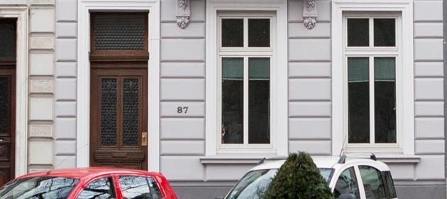 Ein rotes Auto parkt vor einem weißen Gebäude.