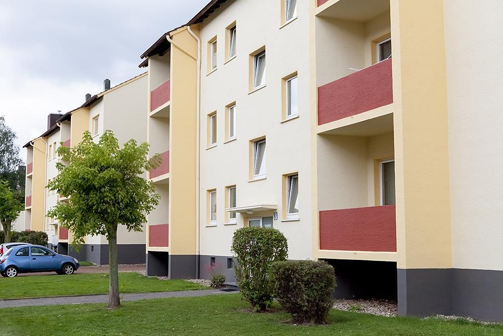 Ein weißes Gebäude mit roten Balkonen und einem davor geparkten blauen Auto