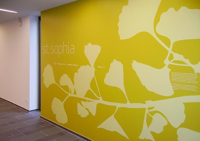 Eine gelbe Wand mit weißen Blättern und dem Wort Sophia darauf