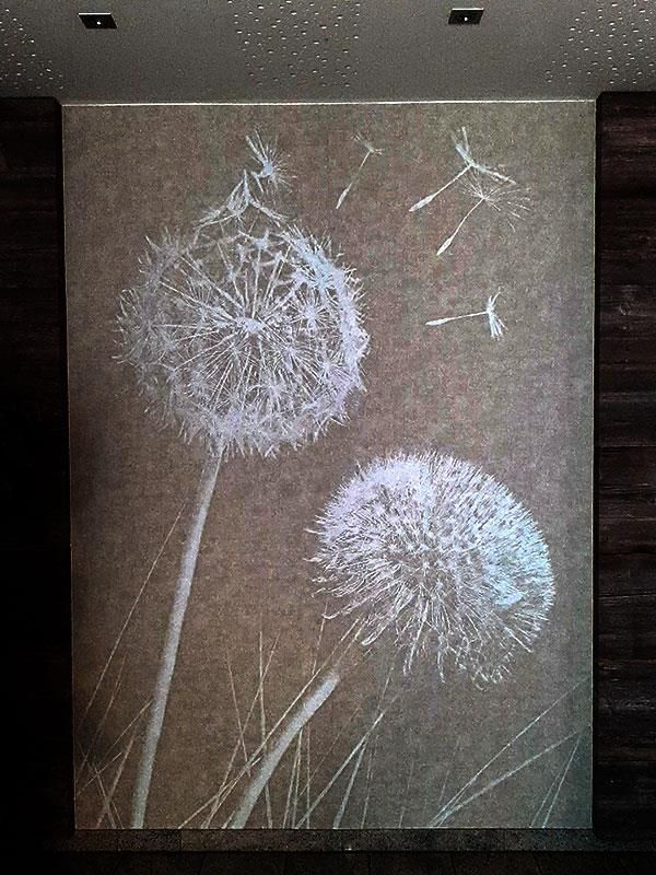 Ein Gemälde von im Wind wehenden Löwenzahnblüten an einer Wand.