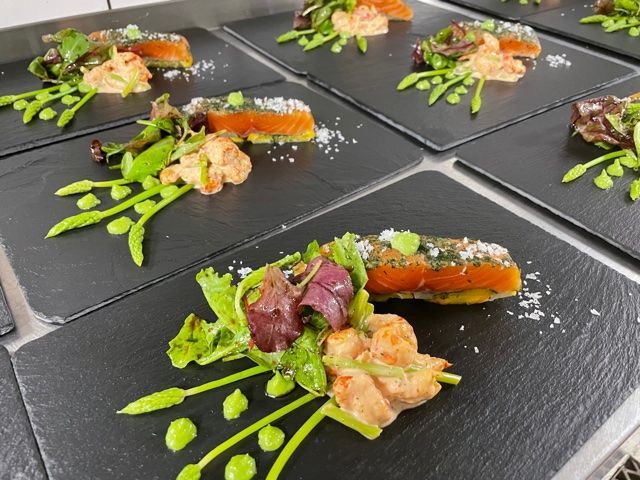 Angerichtetes Lachsgericht mit Gemüse und Soße auf schwarzem Schiefer, servierfertig.