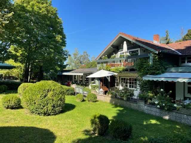 Restaurant „Schützenhaus Grüne“ mit Außenbestuhlung, Frau sitzt an einem Tisch, grüne Büsche und Bäume.