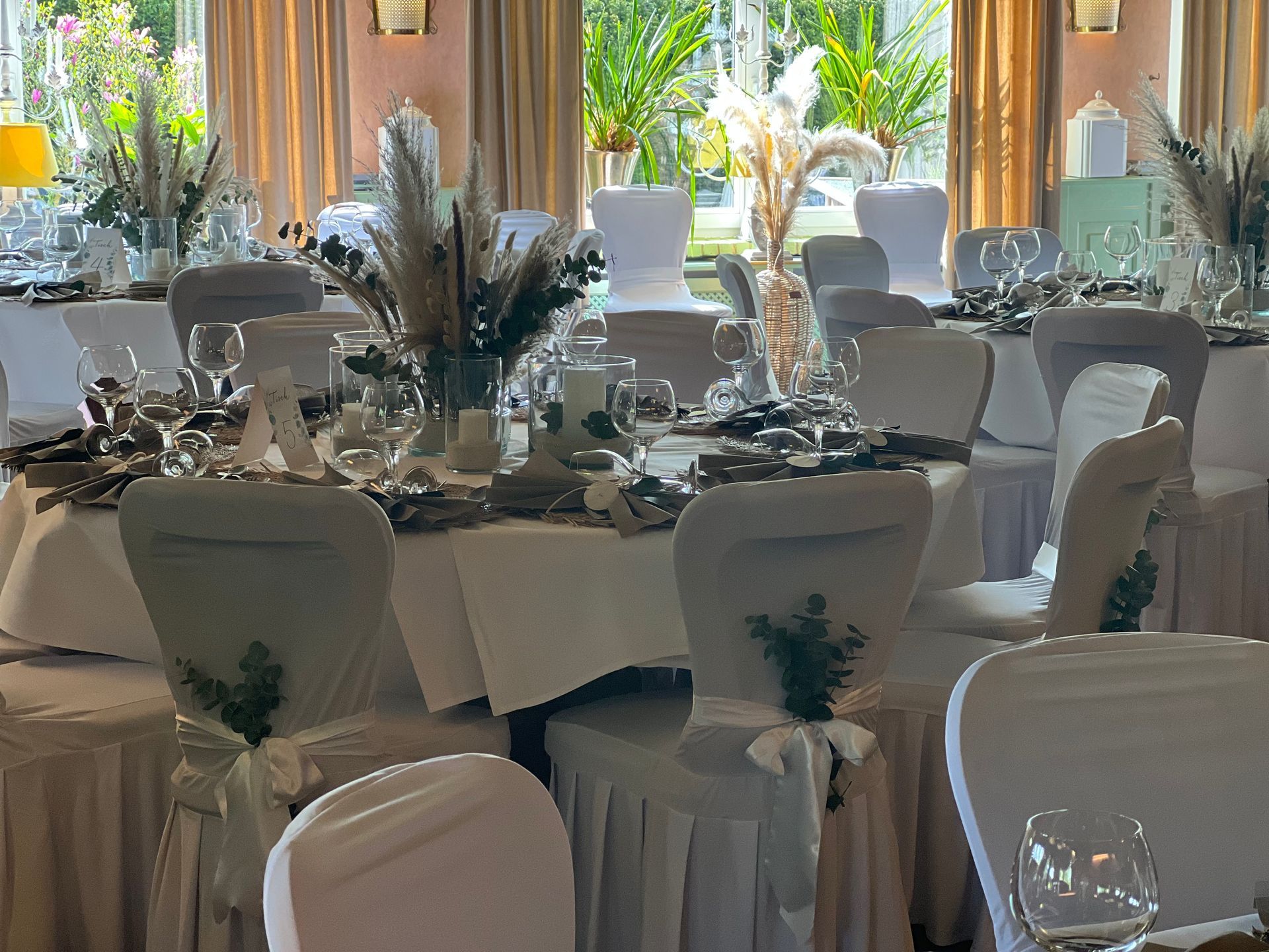 Freiluftrestaurant mit Tischen unter grünen Sonnenschirmen, umgeben von Bäumen und einem Gebäude mit roten Akzenten.