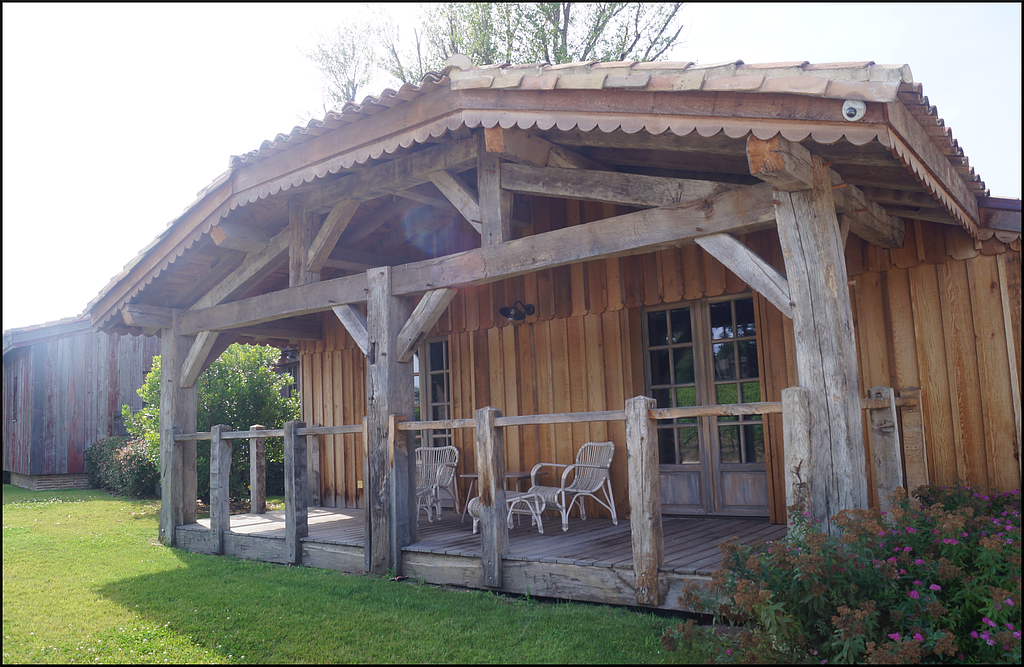 Porche d’une cabane rustique en bois, avec des chaises à bascule blanches et une pelouse