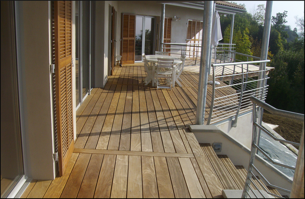 Terrasse de balcon en bois avec garde-corps blanc, chaises de jardin et vue sur les arbres en contrebas