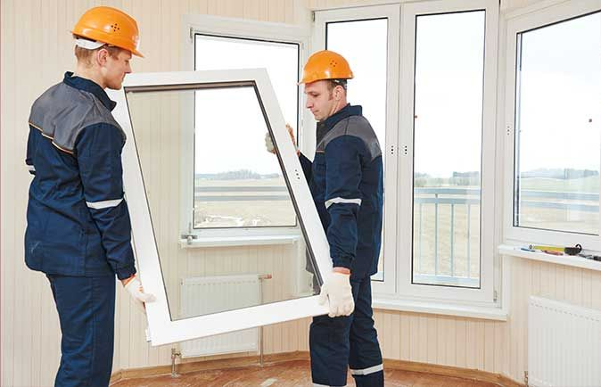 Deux personnes avec un casque orange installant une fenêtre