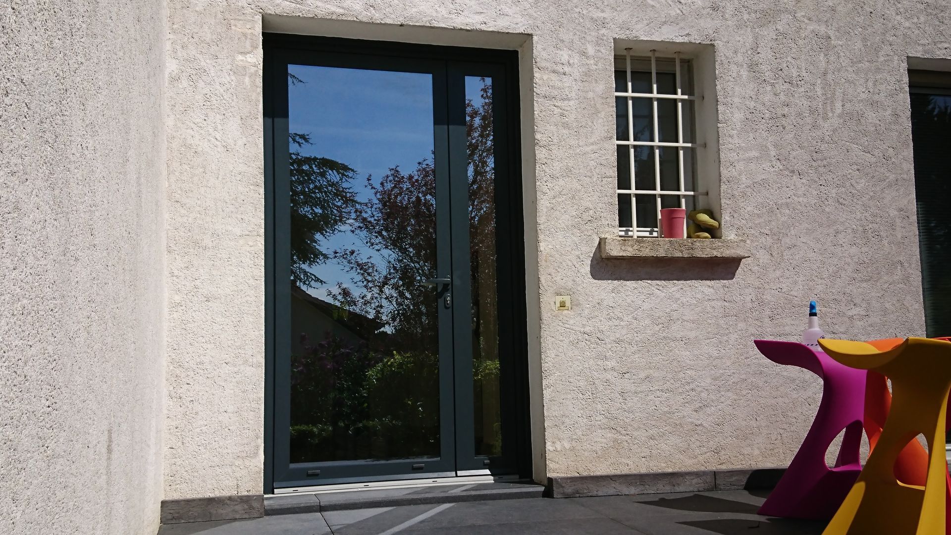 Extérieur d'un bâtiment avec une porte à cadre sombre et une petite fenêtre à barreaux.
