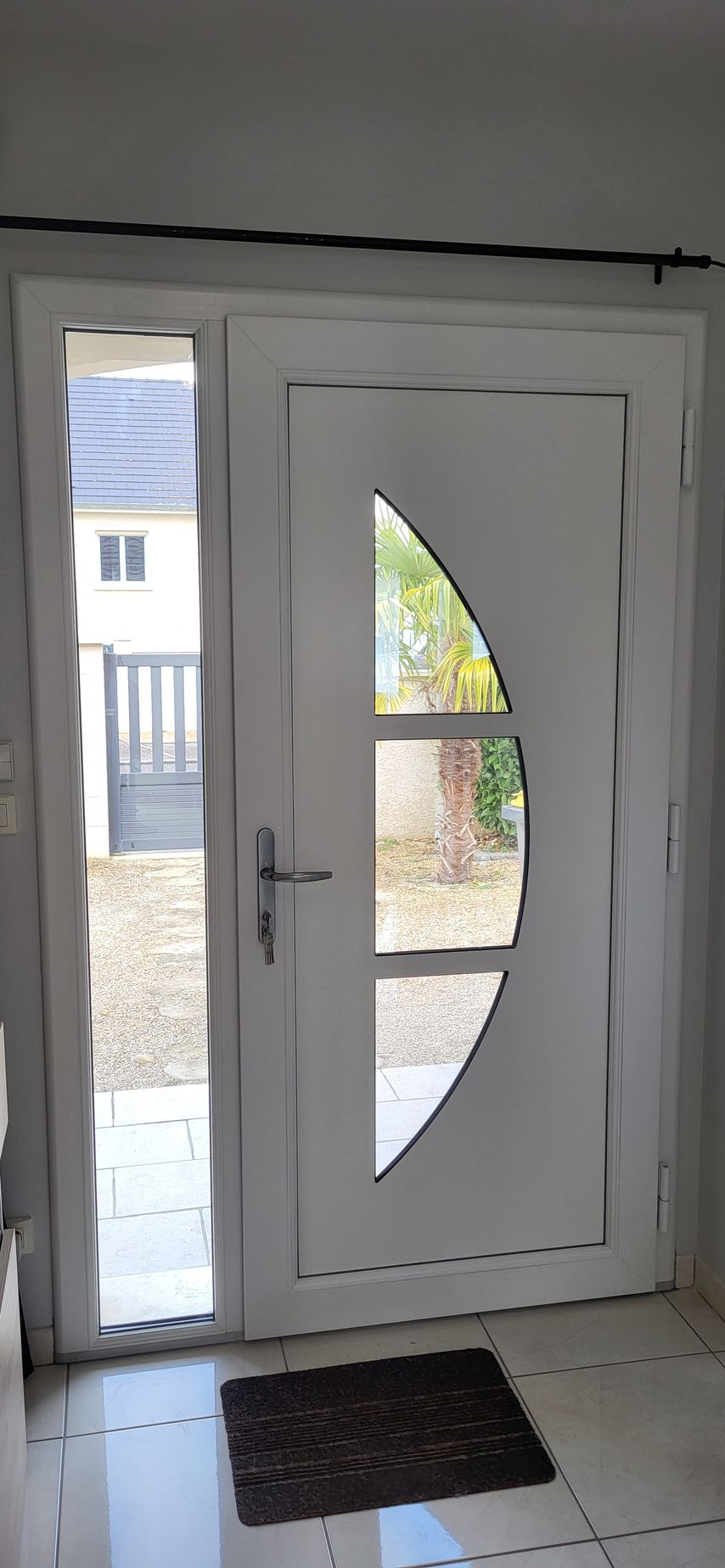Porte d'entrée blanche avec vitres incurvées et un paillasson devant.
