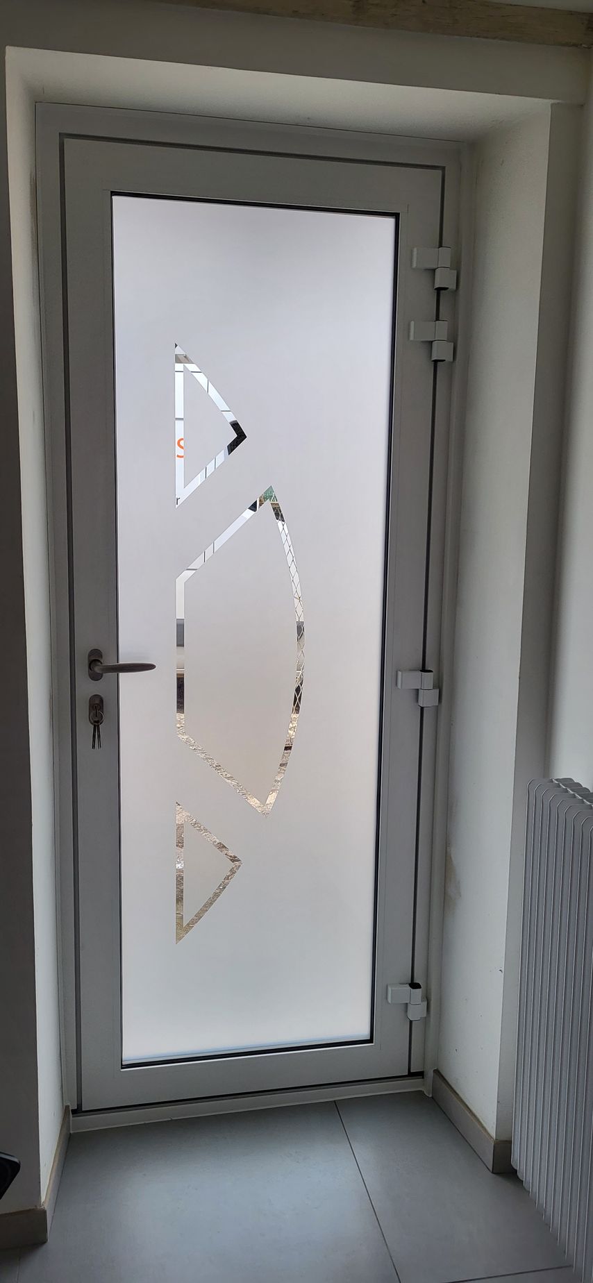 Porte blanche avec verre dépoli et découpes décoratives, encadrée d'un cadre blanc.