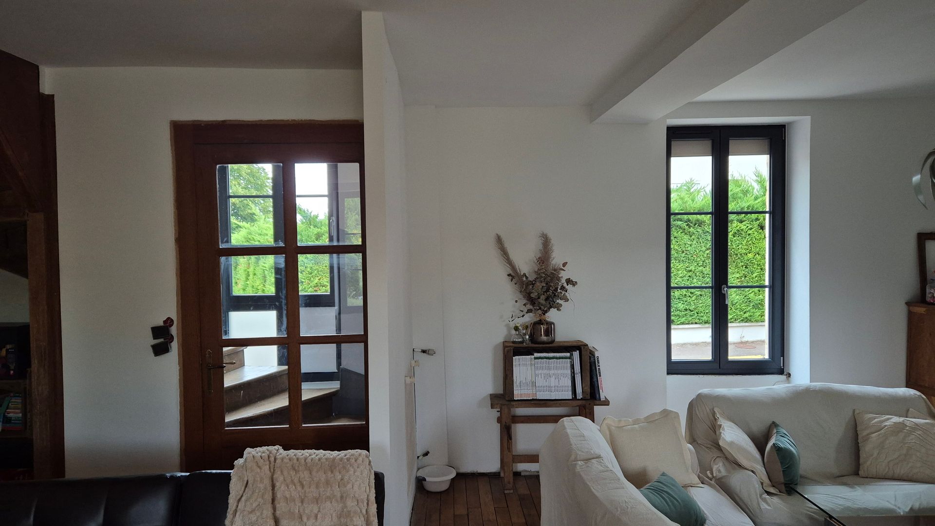 Salon avec porte en bois, murs blancs, deux fenêtres et un canapé.