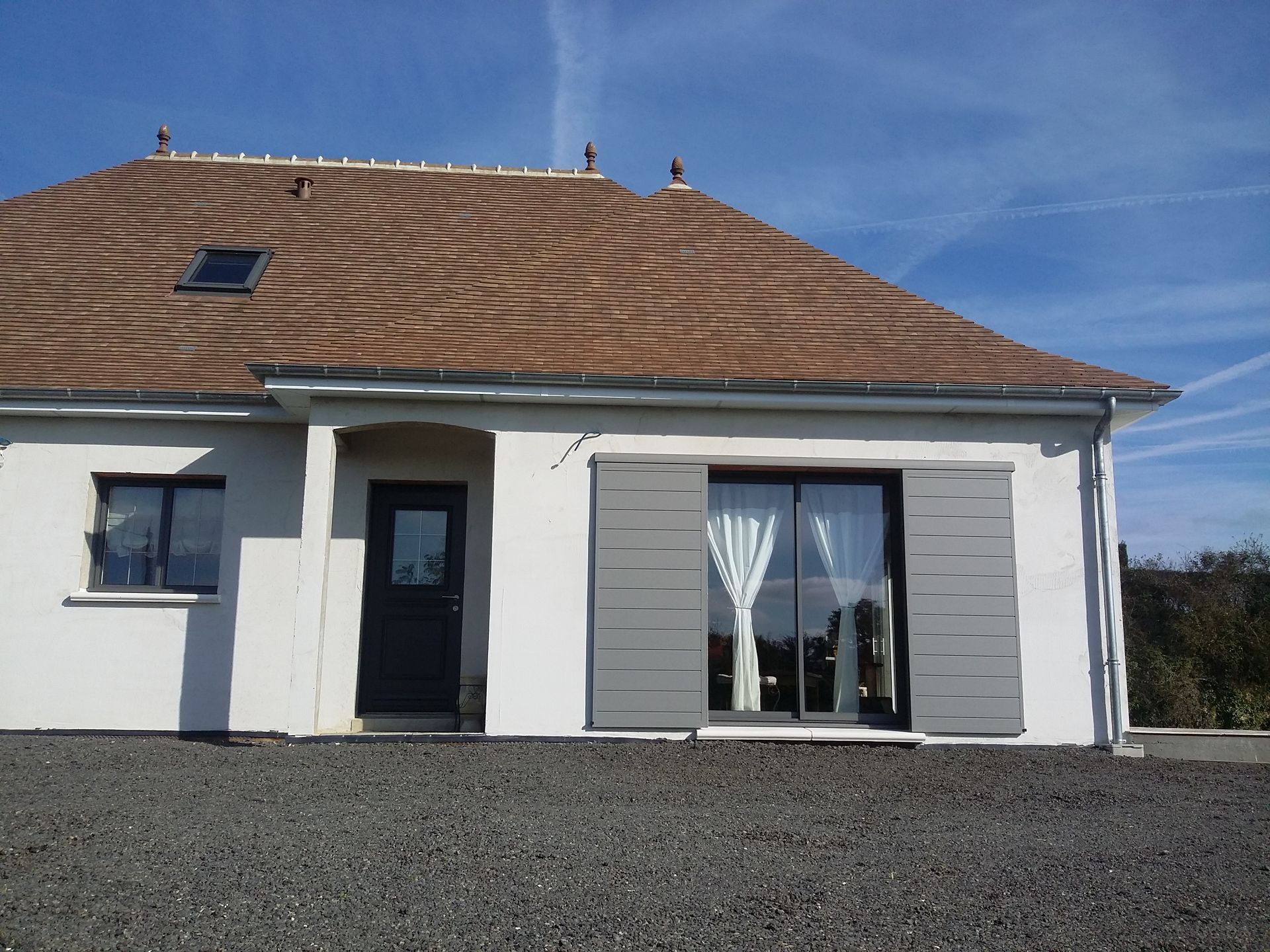 Maison à porte rouge avec volets, porche, fleurs suspendues et buanderie ; extérieur ensoleillé.