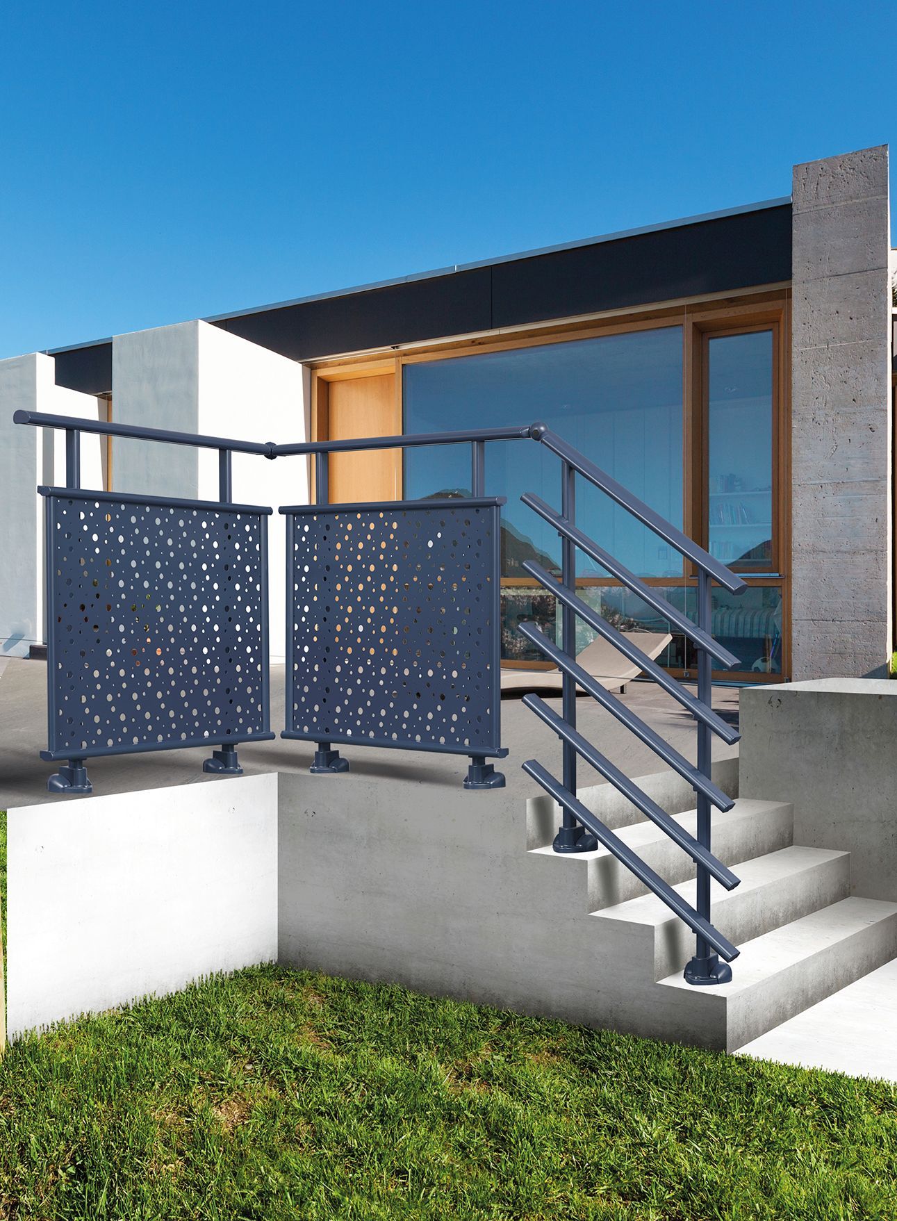 Maison moderne avec rampe d'escalier grise et panneau décoratif. Marches en béton et ciel bleu clair.