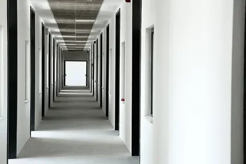 Un largo pasillo en un edificio con paredes blancas y puertas negras.
