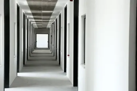 Un largo pasillo en un edificio con paredes blancas y puertas negras.