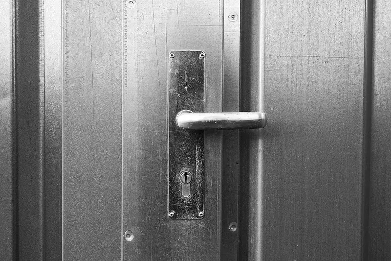 Una fotografía en blanco y negro de una manija de puerta en una puerta de metal.