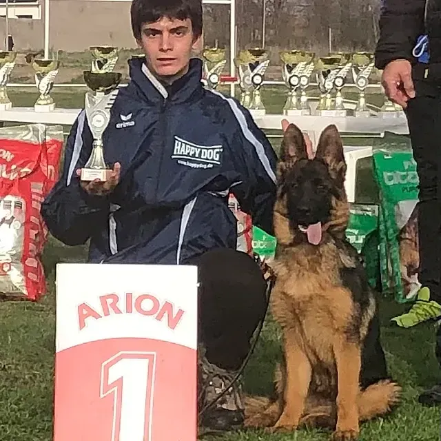 Un hombre sostiene un trofeo junto a un perro pastor alemán.