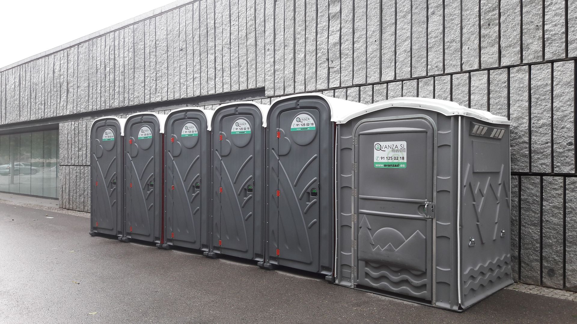 Una fila de baños portátiles están alineados frente a un edificio.
