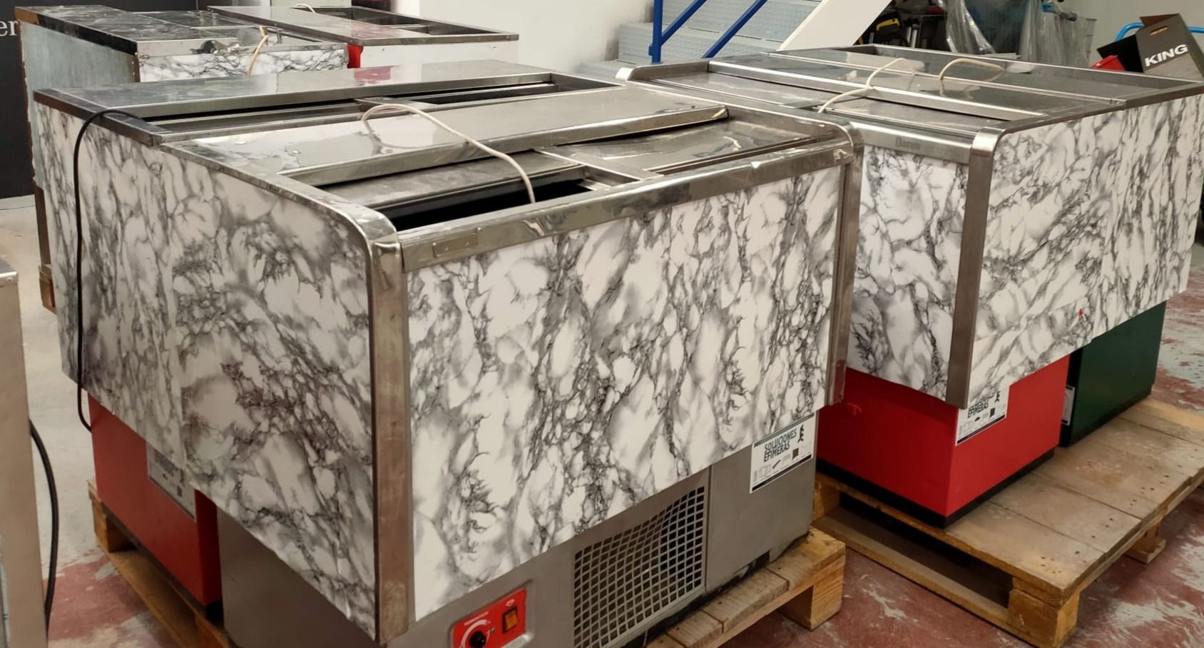 Hay dos refrigeradores sobre paletas de madera en un almacén.