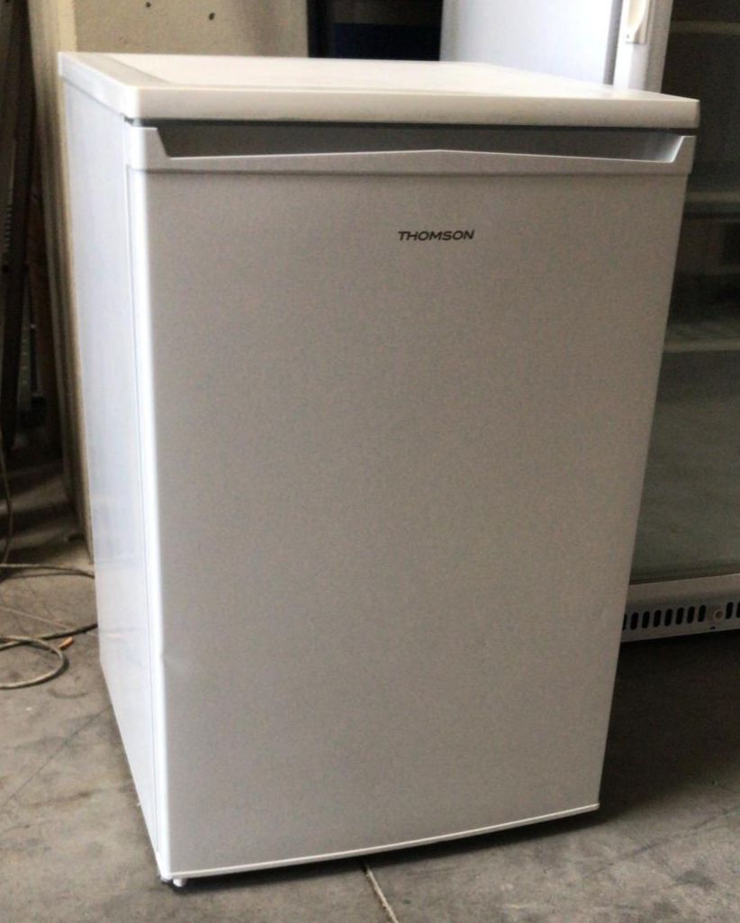 Un refrigerador Thomson blanco se encuentra sobre un piso de concreto.