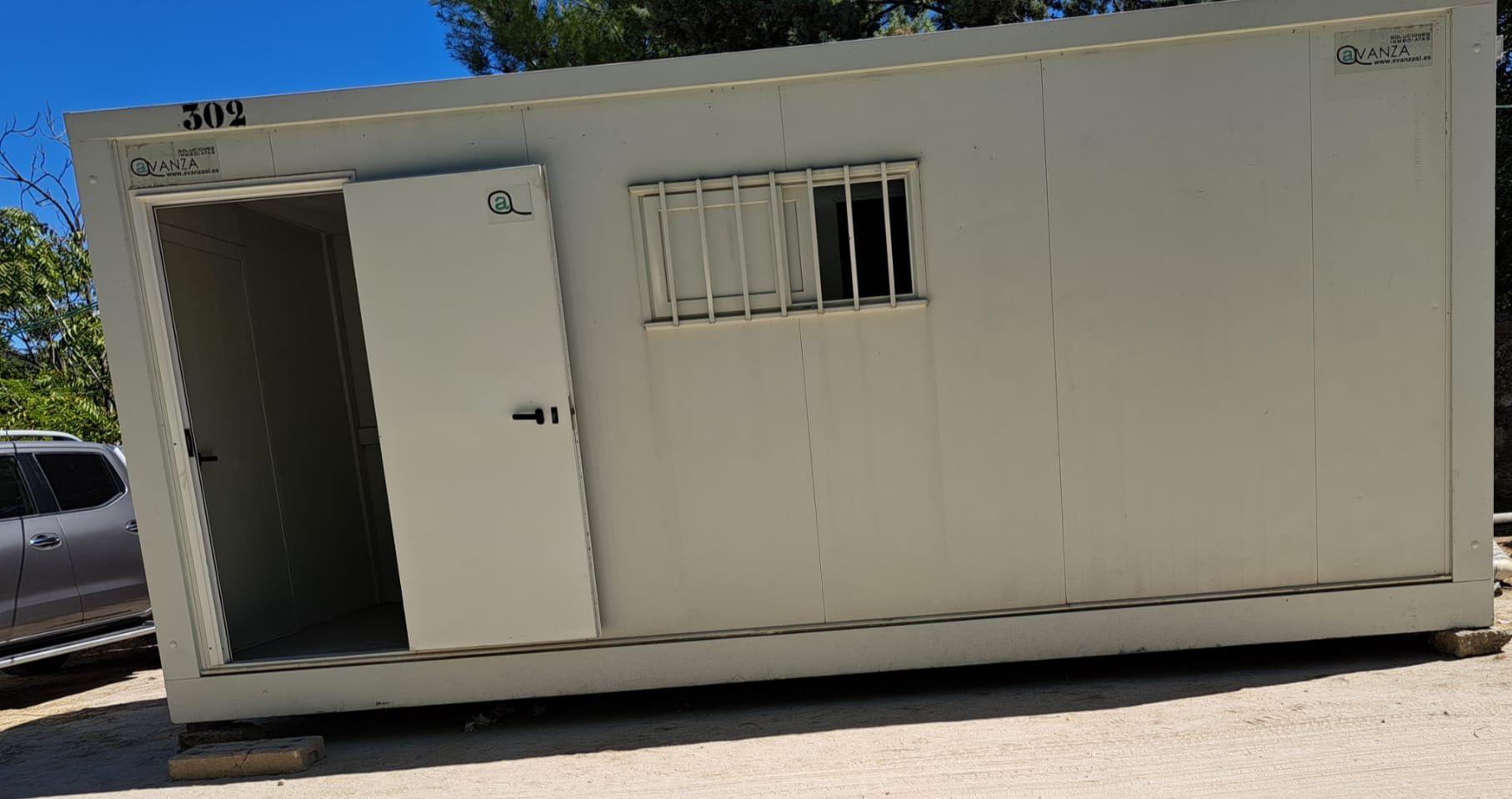 Un contenedor blanco con una ventana y una puerta está estacionado en un estacionamiento.