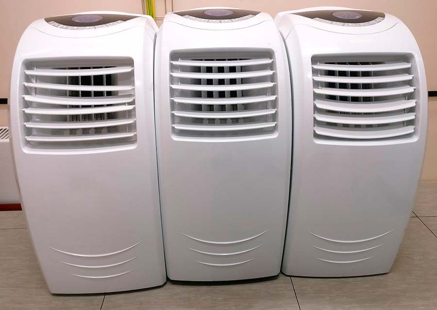 Tres aires acondicionados portátiles blancos están alineados uno al lado del otro