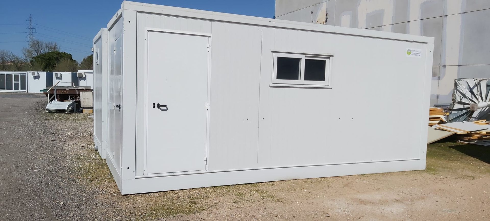 Un edificio blanco con dos ventanas está sentado en un lote de grava.