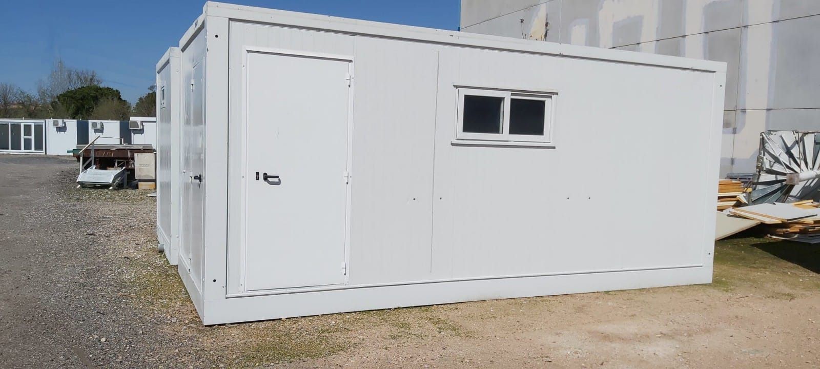 Un edificio blanco con dos ventanas está sentado en un lote de grava.
