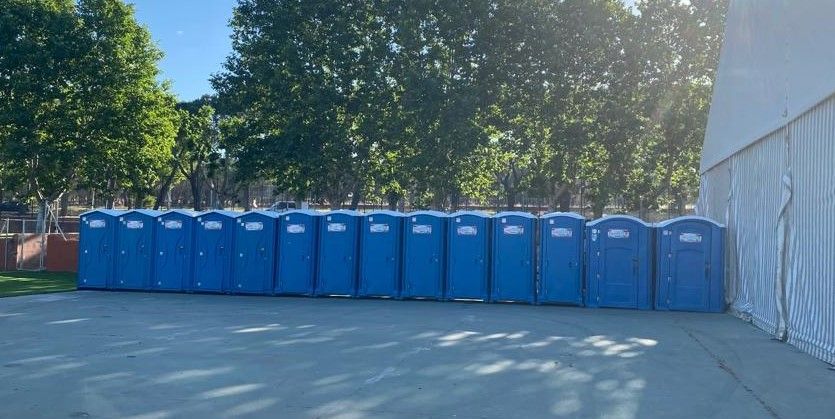 Una fila de baños portátiles azules están alineados en un estacionamiento.