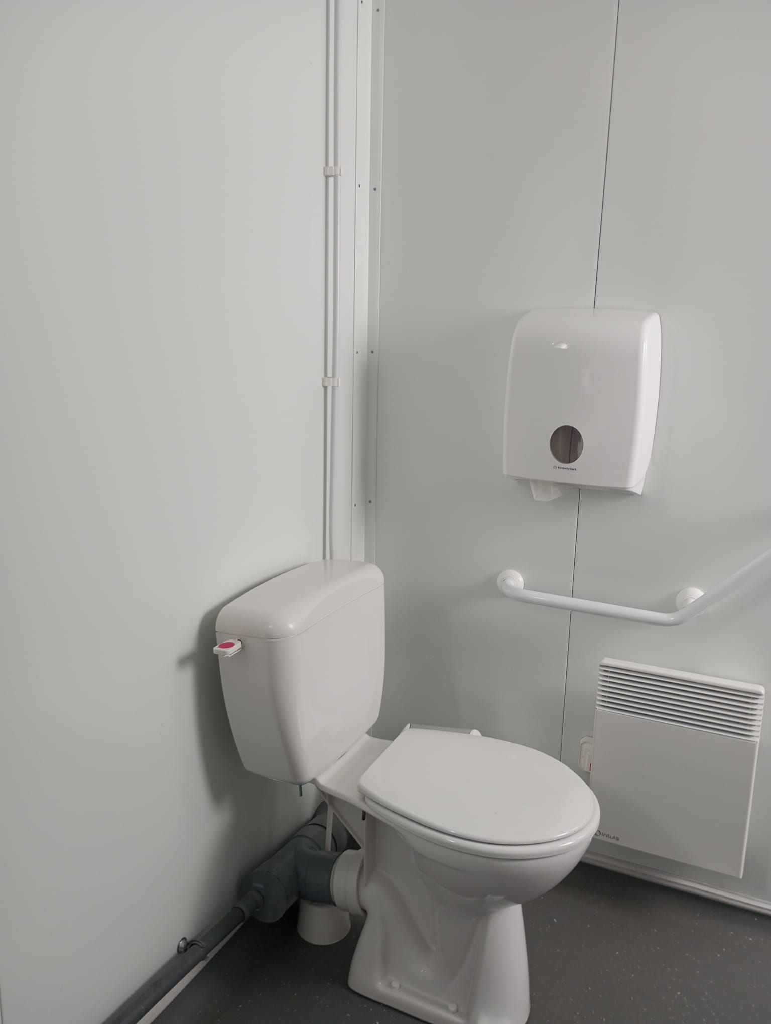En un baño hay un inodoro al lado de un dispensador de toallas de papel.