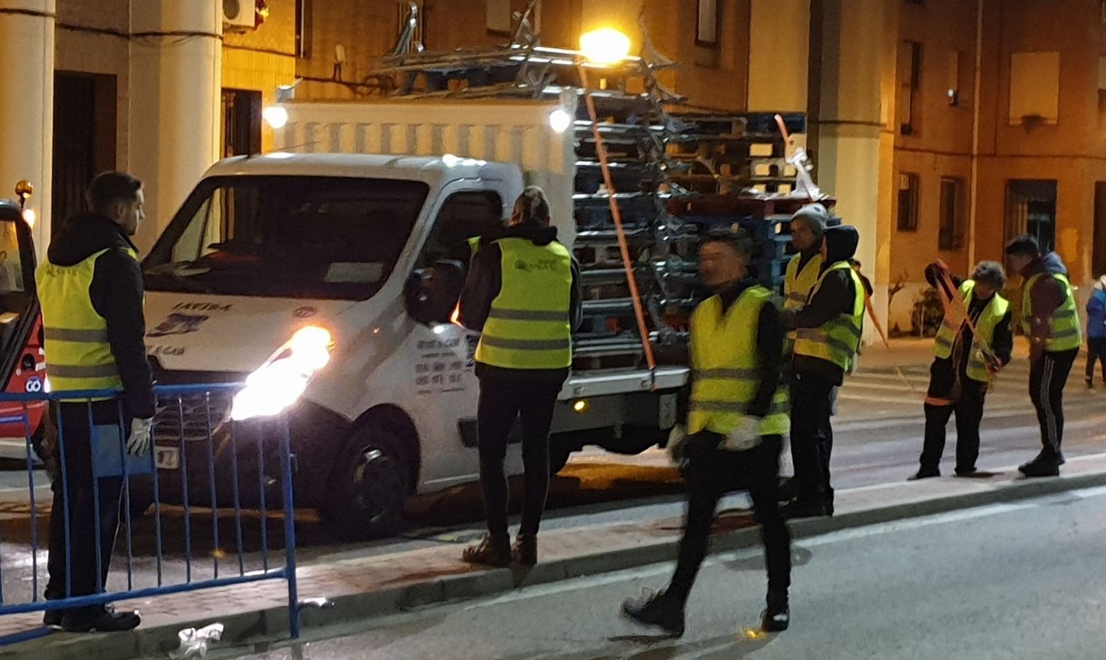 Un grupo de personas que visten chalecos amarillos están de pie frente a una camioneta blanca.