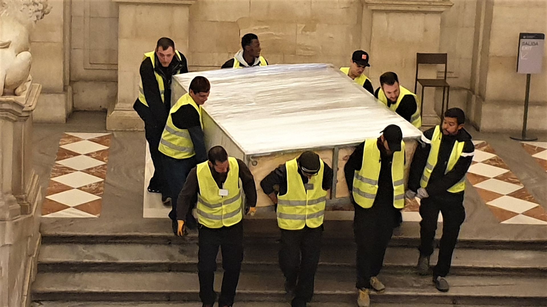 Un grupo de hombres con chalecos amarillos llevan un gran trozo de madera.