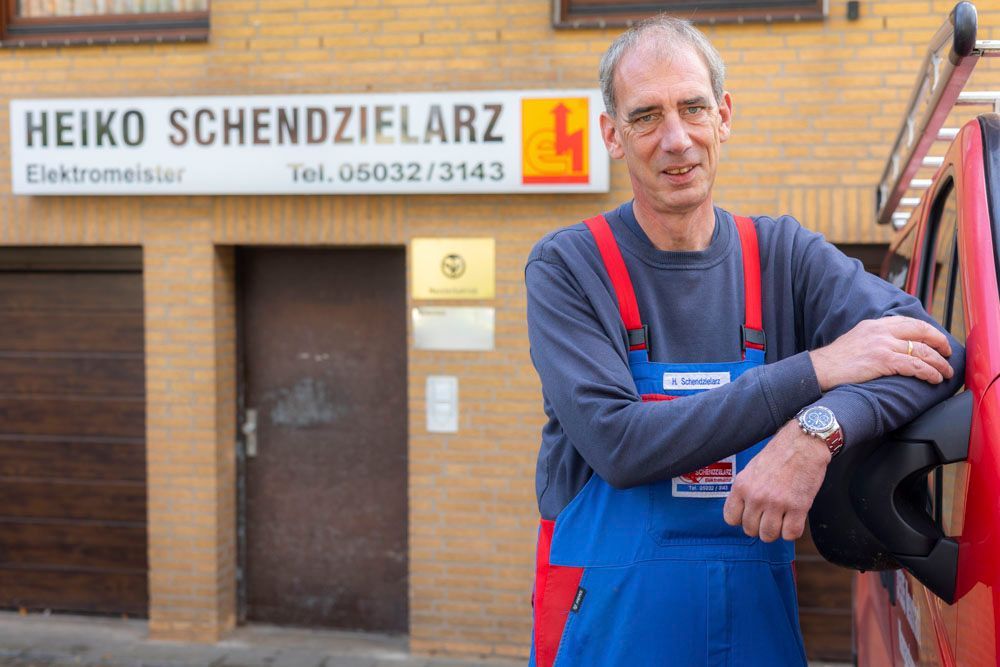 Man in work clothes poses next to a red van; sign reads 