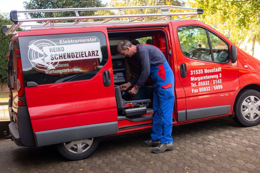 Roter Lieferwagen mit offener Tür; Elektriker arbeitet an Werkzeugkästen. Aufschrift auf dem Lieferwagen: 