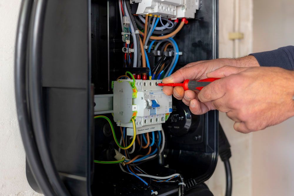 Ein Elektriker arbeitet mit einem Schraubendreher an einem Schaltschrank. Drähte und Bauteile sind im Inneren des schwarzen Schaltschranks sichtbar.
