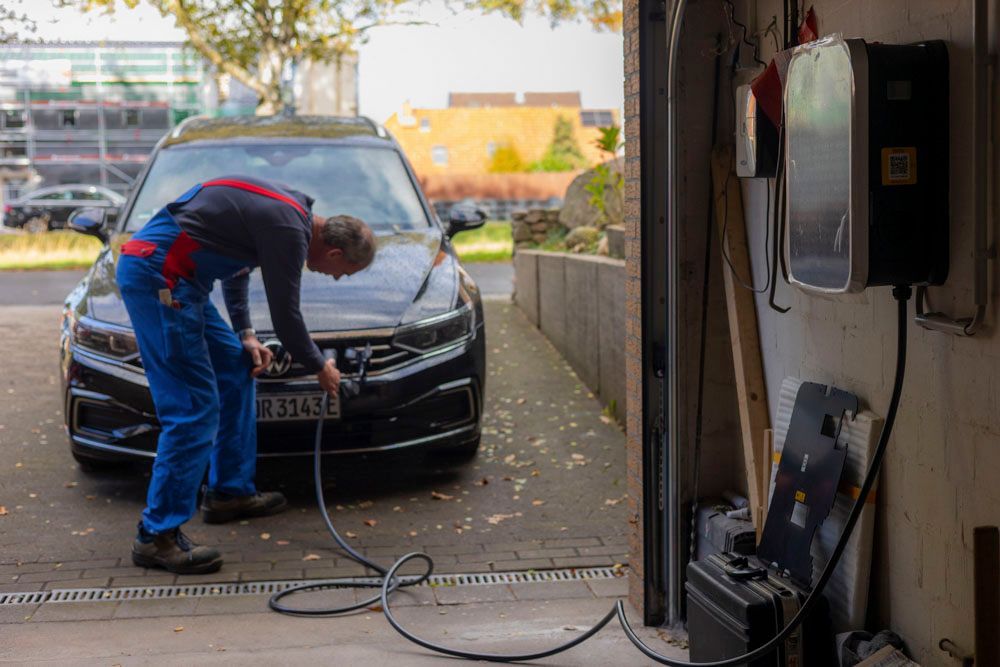 Ein Mann steckt ein Ladekabel in ein schwarzes Elektroauto, das in einer Garage geparkt ist.