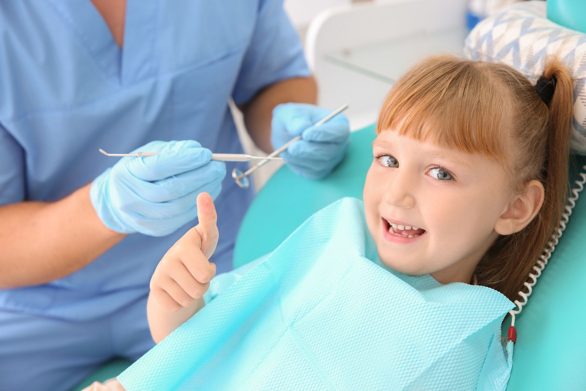 ein kleines Mädchen sitzt in einem Zahnarztstuhl und gibt einen Daumen nach oben