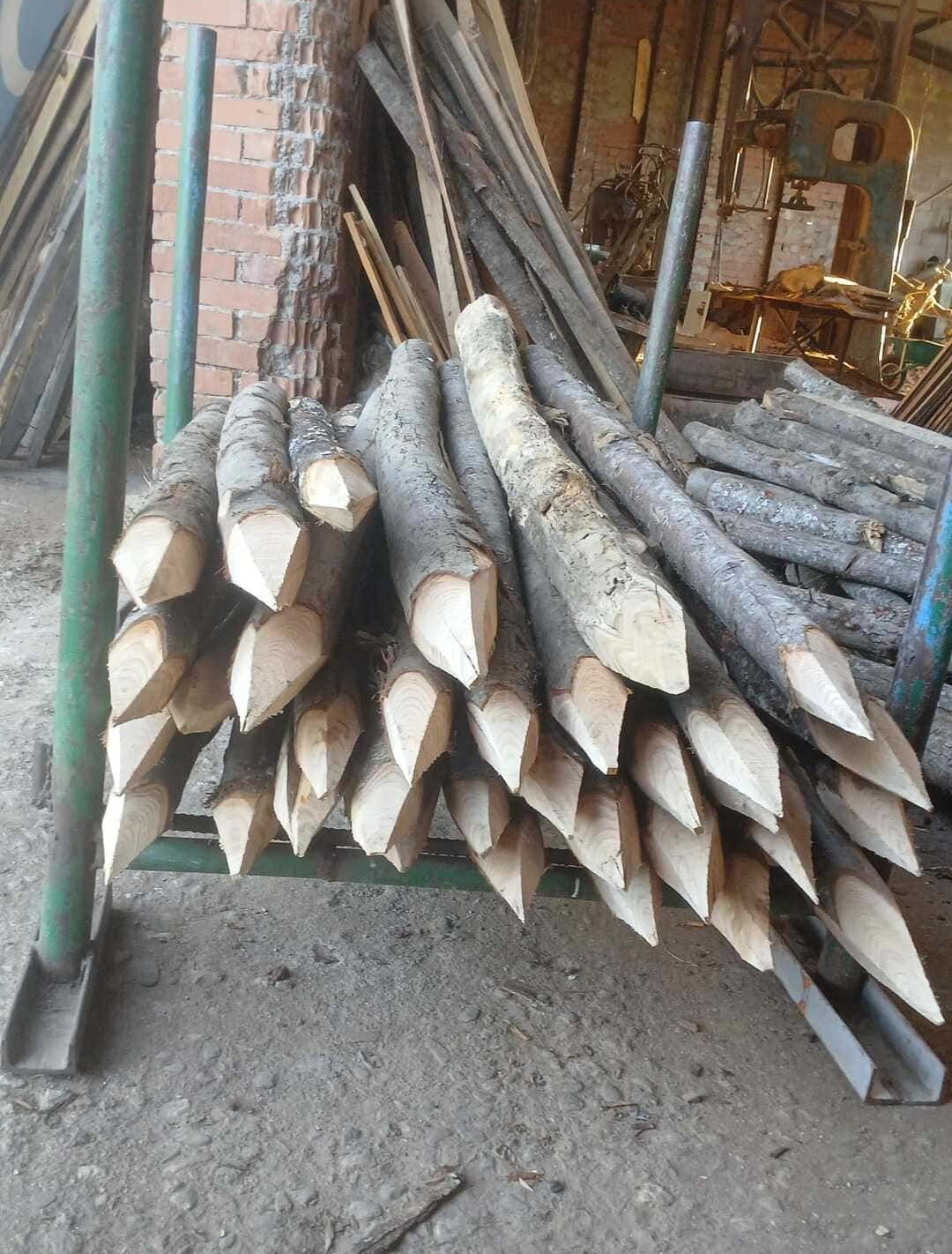 Postes de madera cortados apilados e inclinados sobre un soporte metálico al aire libre.