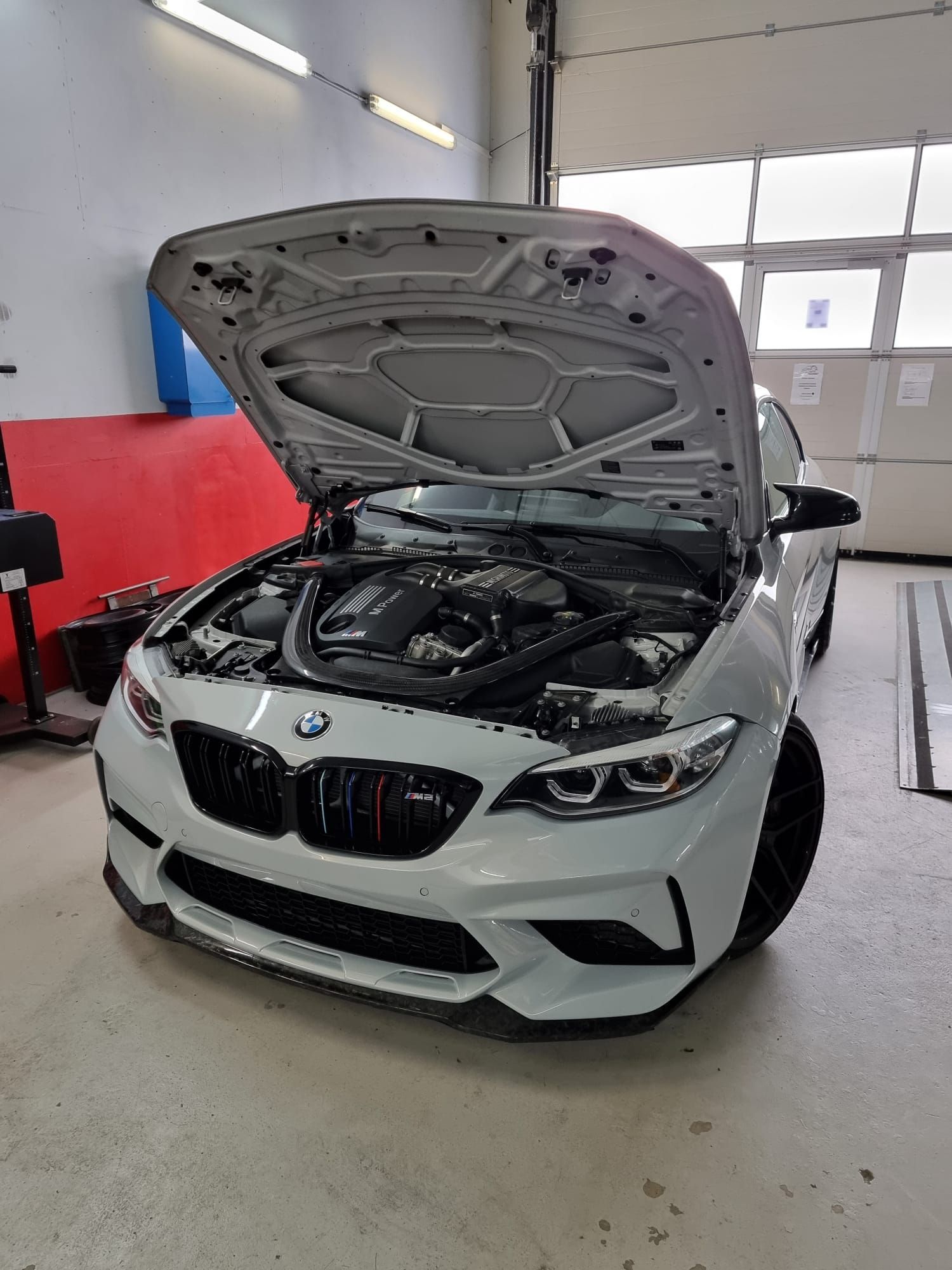 Voiture de sport BMW blanche, capot ouvert, dans un garage, laissant apparaître le compartiment moteur.