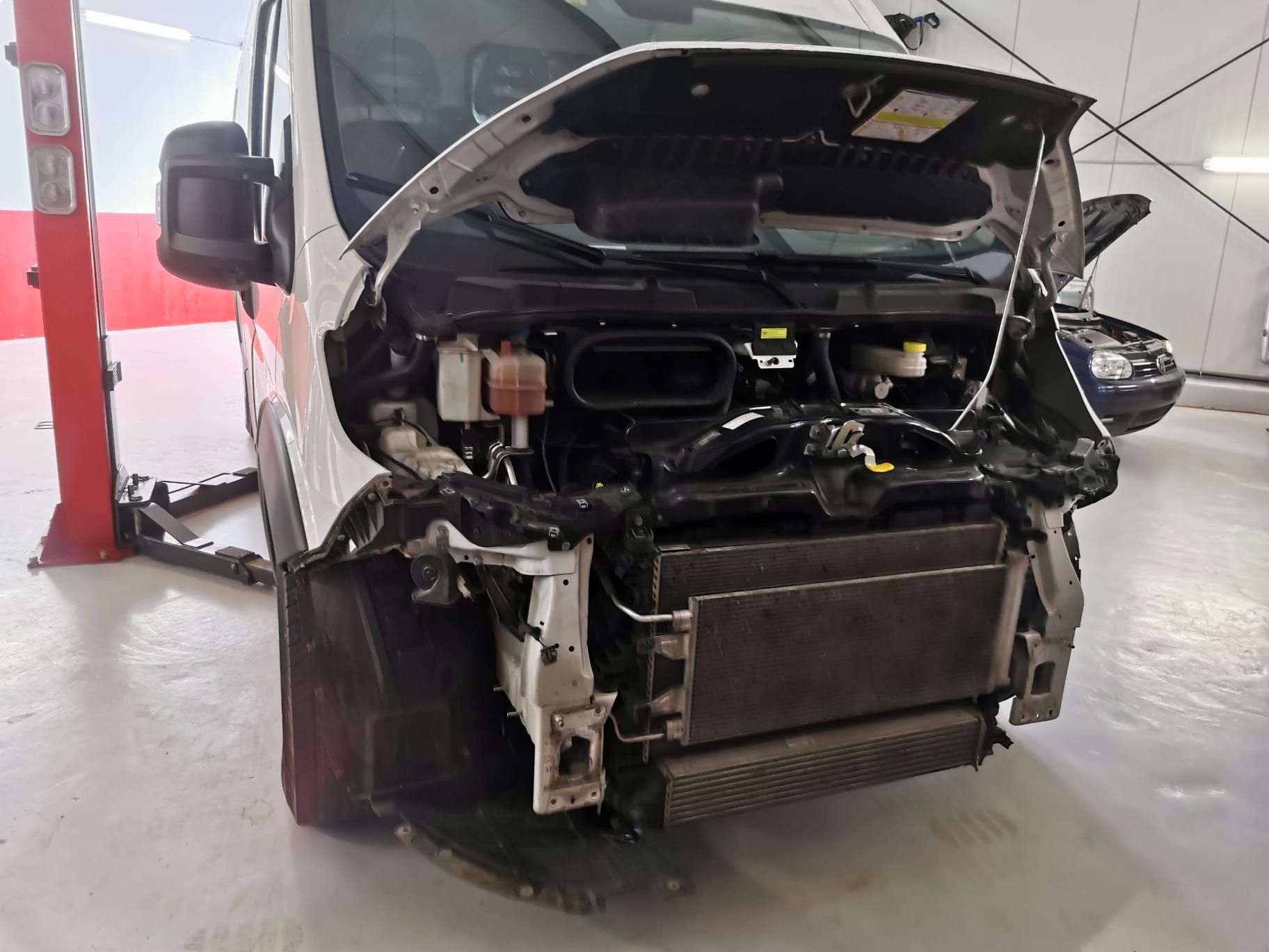 Atelier de réparation automobile avec plusieurs voitures, un mécanicien près d'un véhicule blanc.