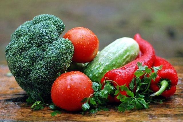 Brócoli, tomates, pimientos, pepinos y perejil están sobre una mesa de madera.