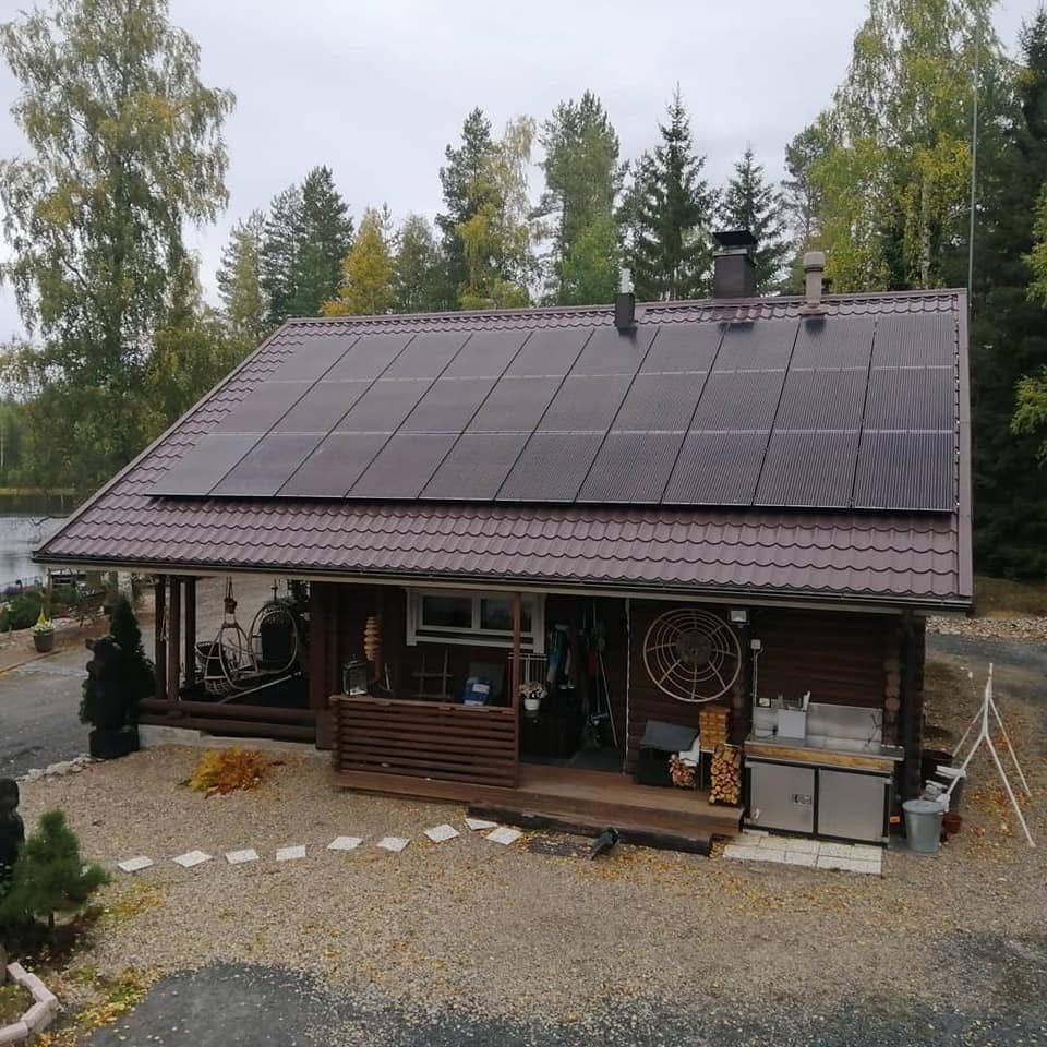 Hirsimökki, jossa on suuri aurinkopaneelikatto, sorapiha ja puita rauhallisessa metsäisessä ympäristössä
